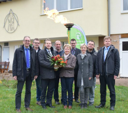 Bürgermeister Junghans (l.) und Jörg Hartmann, Geschäftsführer EnergieNetz Mitte (3. v. l.), überreichen der ersten Kundin am Gasnetz Blumen. 