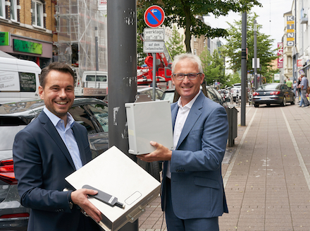 Oberbürgermeister David Langner (l.) und evm-Vorstandsvorsitzender Josef Rönz zeigen die Luftsensoren, die in Kürze an Laternenmasten entlang der Löhrstraße montiert werden, um die Luftqualität zu messen.
