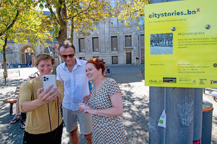 Oberbürgermeisterin Katja Dörner (l.) lässt sich von Videokünstlerin Annika Ley und dem Leiter des Fringe-Ensembles, Frank Heuel, die App City Stories Bonn vorführen.