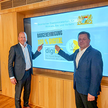 Landrat Martin Sailer (links) und Staatsminister Christian Bernreiter freuen sich über Bayerns erste digital versendete Baugenehmigung in Augsburg.