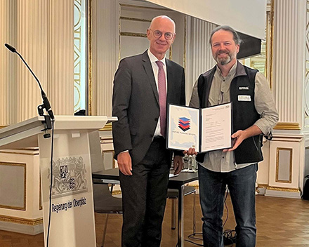 Regierungspräsident Walter Jonas (r.) überreicht Dr. Ulrich Huber vom Landratsamt Cham die Anerkennung des Bayerischen Staatsministeriums für Wohnen, Bau und Verkehr.